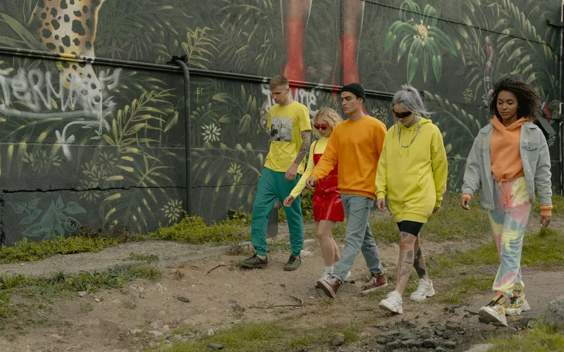 A group of trendy young adults walking by a vibrant urban mural, showcasing street style fashion.