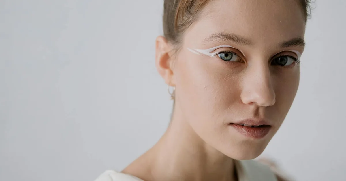 Close-up portrait of a woman with unique white eye makeup and minimalist background.
