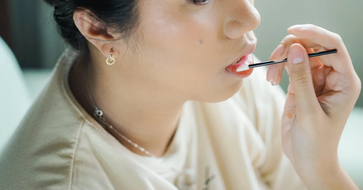 Close-up of a woman applying makeup with a brush, showcasing her lips.