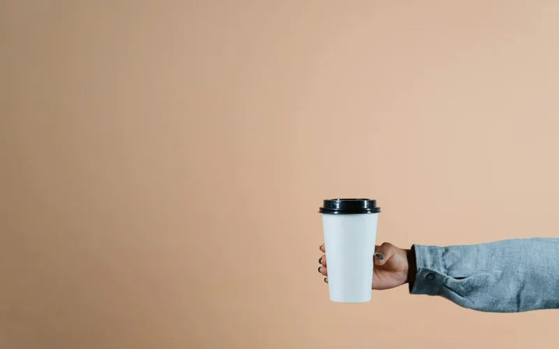 A simple photo of a hand holding a coffee cup against a beige background with copyspace.