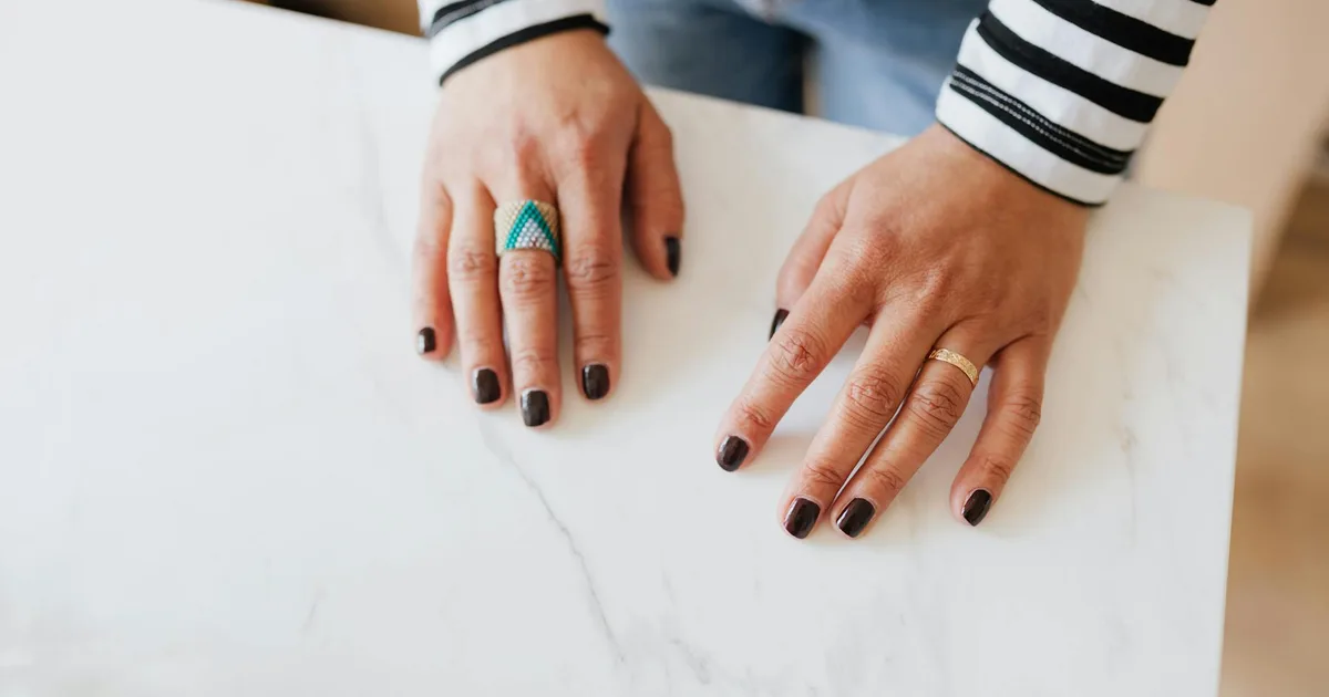 From above unrecognizable woman demonstrating hands with manicured nails on white table in apartment during weekend