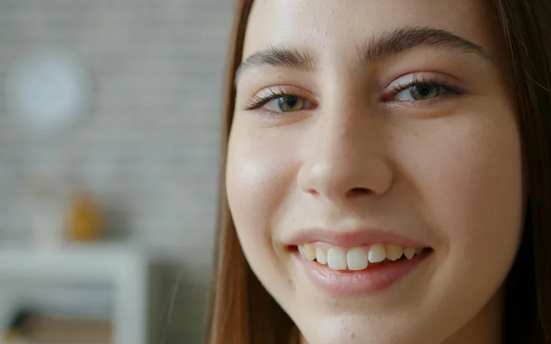 Close-up of a smiling young woman with clear skin indoors.
