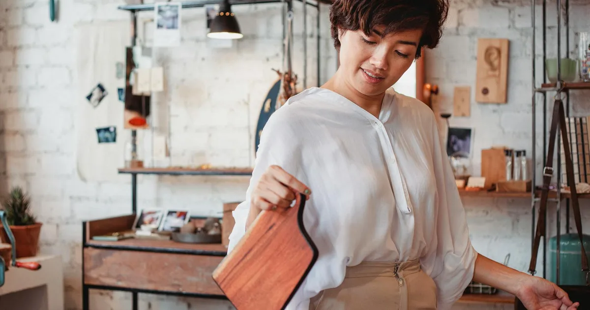 Young content ethnic female shopper with wooden cutting board in store with brick wall