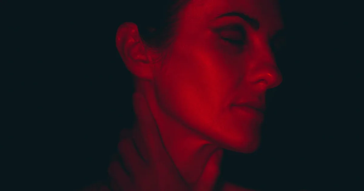 Close-up portrait of a woman with eyes closed, illuminated by red light, creating a moody and artistic atmosphere.
