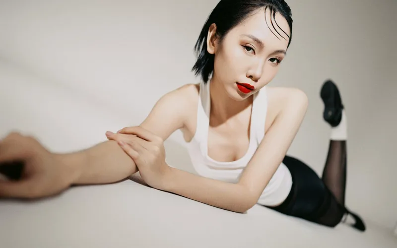 Portrait of a fashionable woman in a white tank top and red lipstick, stretching elegantly.