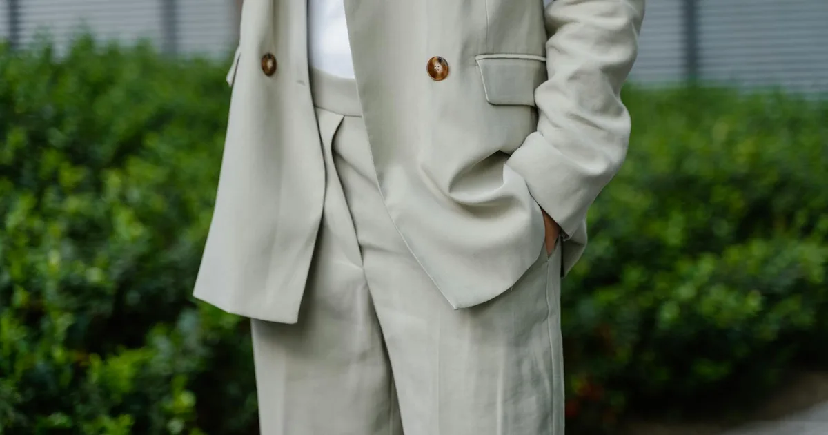 Close-up of an unrecognizable person wearing a stylish beige suit with hands in pockets outdoors.