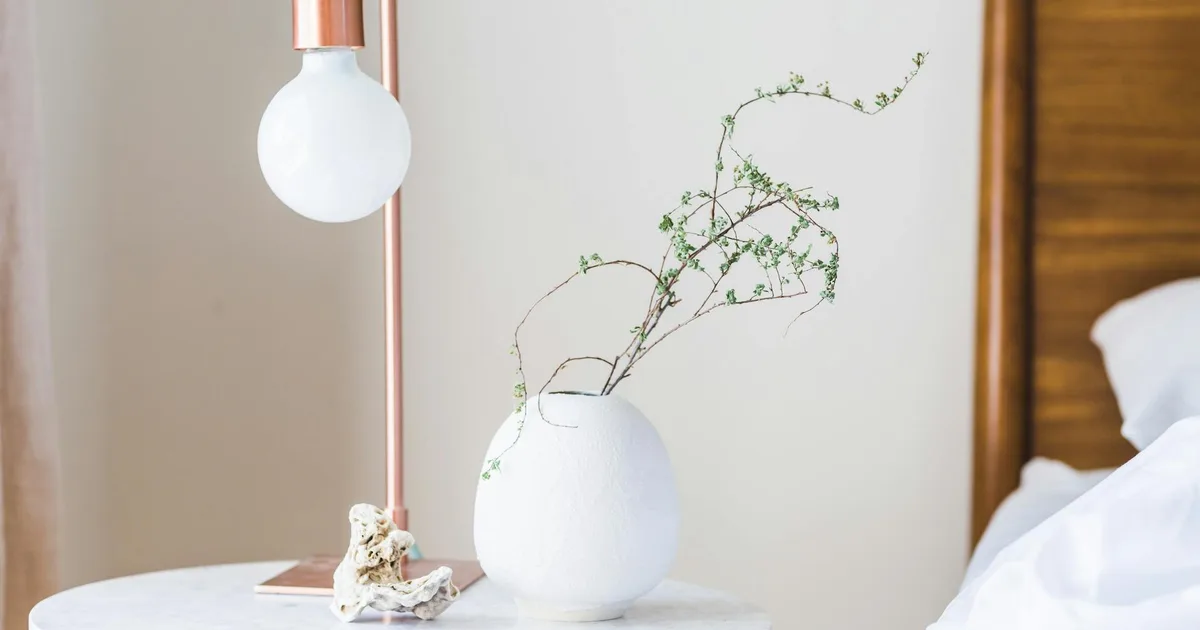 Stylish bedroom with a minimalist lamp and vase on a marble side table.