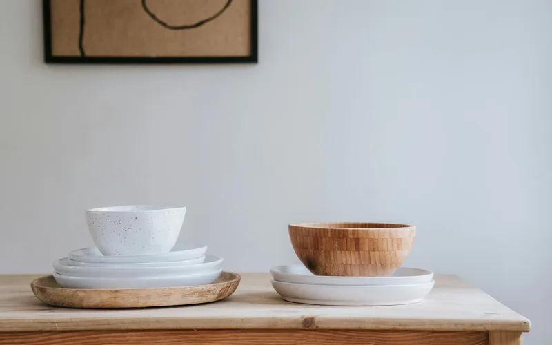 Minimalist setup of white and wooden bowls on a wooden table with abstract artwork.