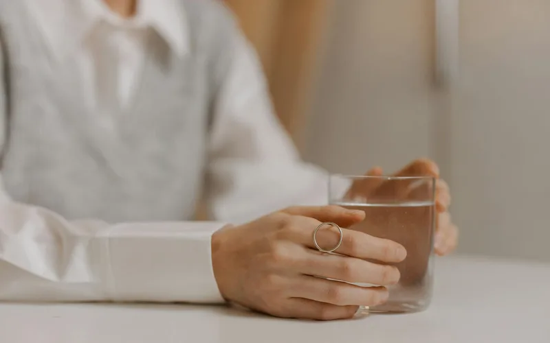 Elegant hands holding a glass of water on a table with a soft focus background.