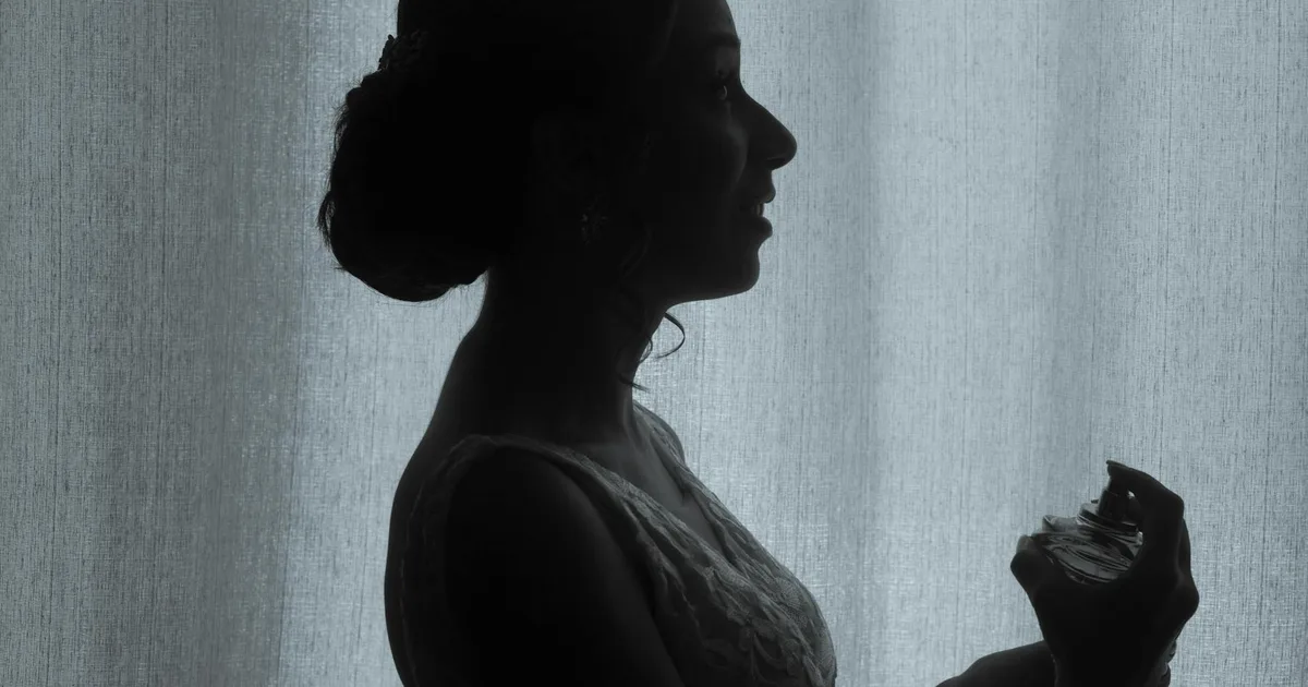 Silhouette of a bride applying perfume, elegant and timeless in natural light.