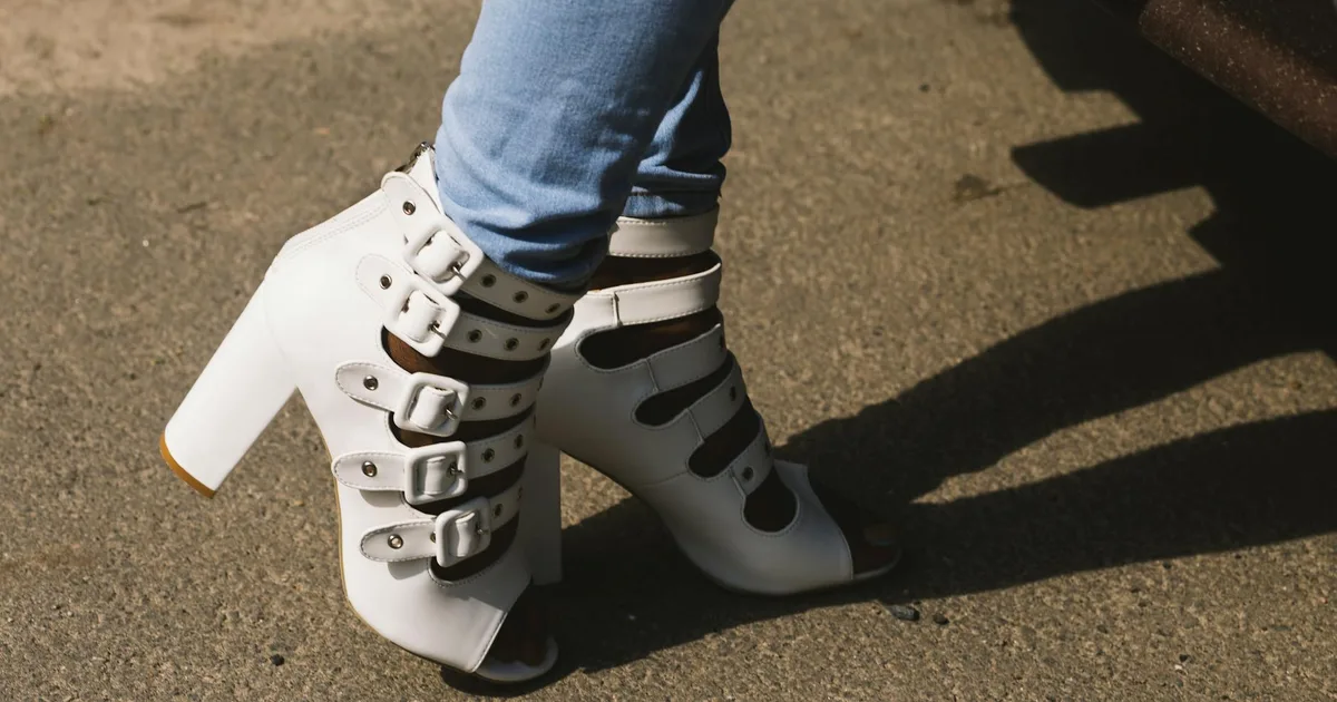 Close-up of a woman's legs in white high-heeled sandals and jeans on the street pavement.