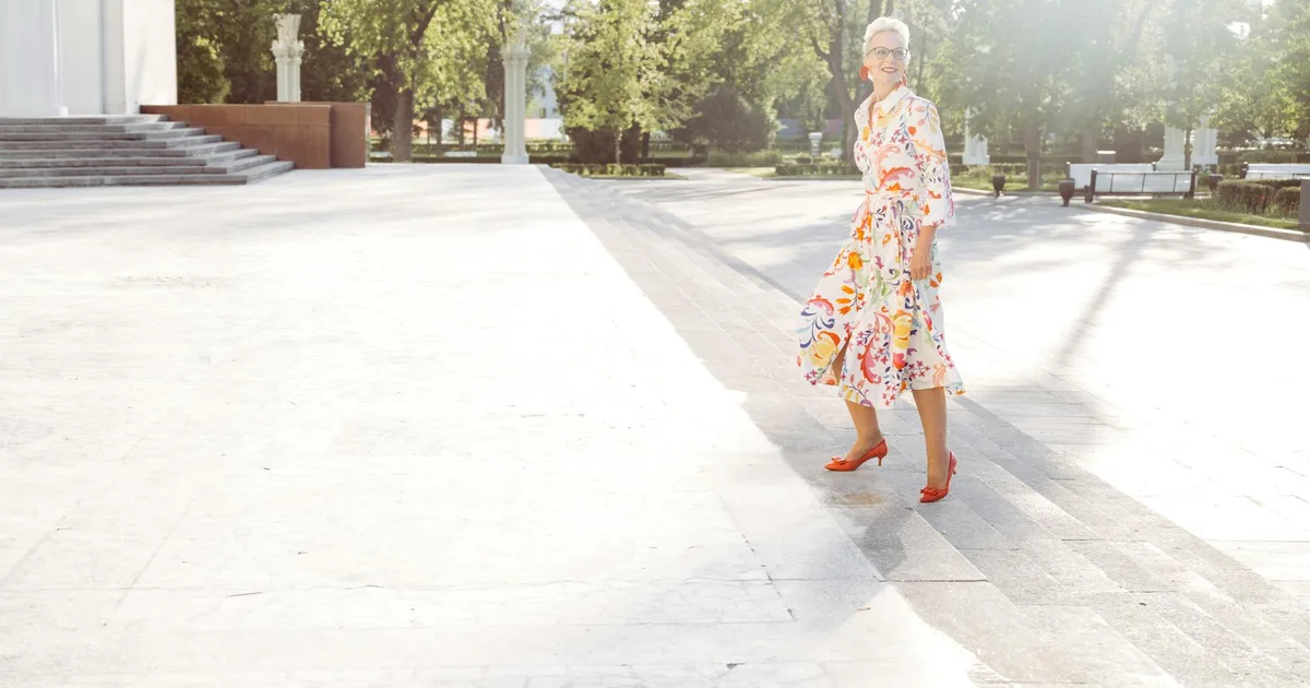 A fashionable senior woman in a vibrant dress walking outdoors on a sunny day.