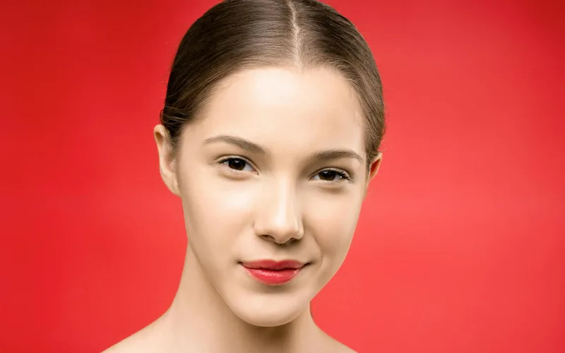 A young woman with red lipstick poses gracefully against a vibrant red backdrop.
