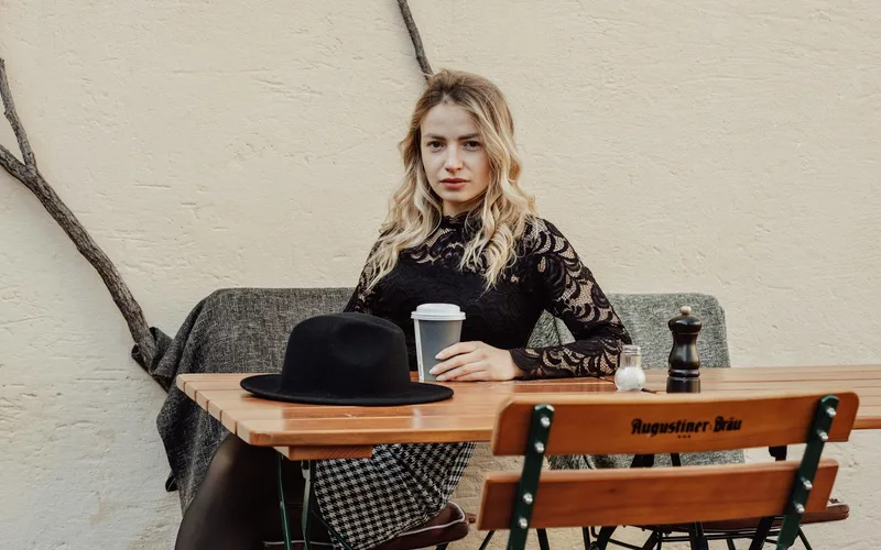 Model in a black lace blouse and checkered skirt seated at an outdoor cafe table.
