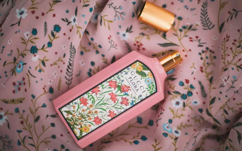 A vibrant pink Gucci Flora perfume bottle resting on a floral patterned fabric, showcasing elegance and style.