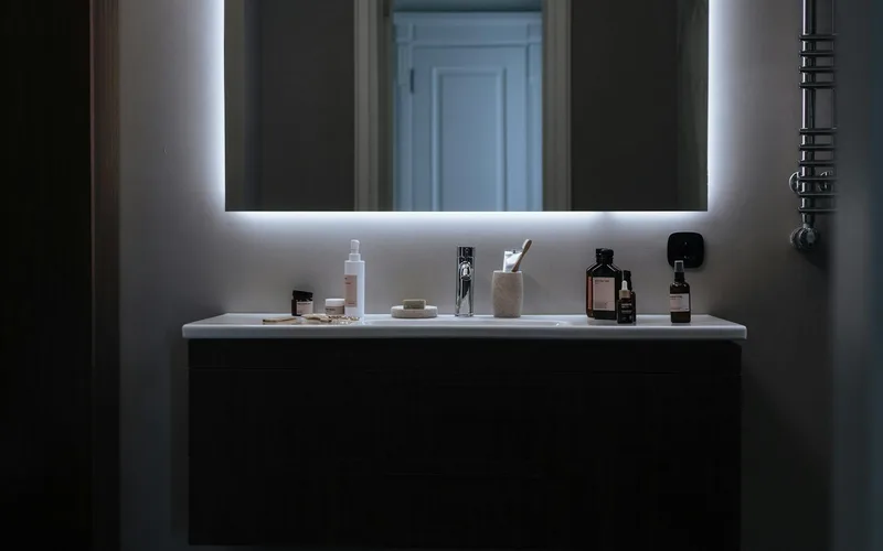 Sleek bathroom vanity setup with LED mirror and various cosmetic products against a modern backdrop.