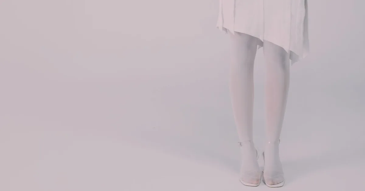 Close-up of a woman's legs wearing a white dress and high heels in a studio setting.