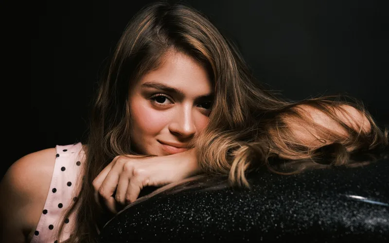 Captivating portrait of a young woman with long hair and a gentle smile, set against a dark background.