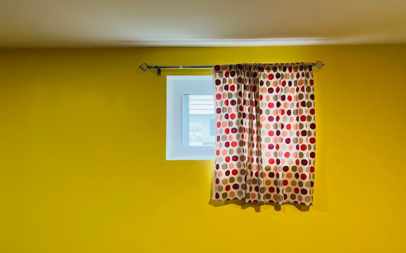 A vivid yellow wall featuring a window adorned with red and black polka dot curtains.