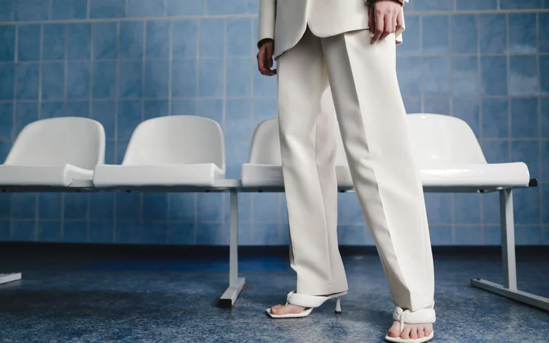 A stylish woman in a white suit and sandals standing in a modern waiting room.