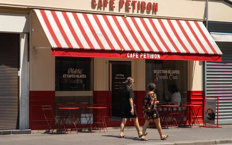 A classic Parisian café with red striped awning and people walking by on a sunny day.