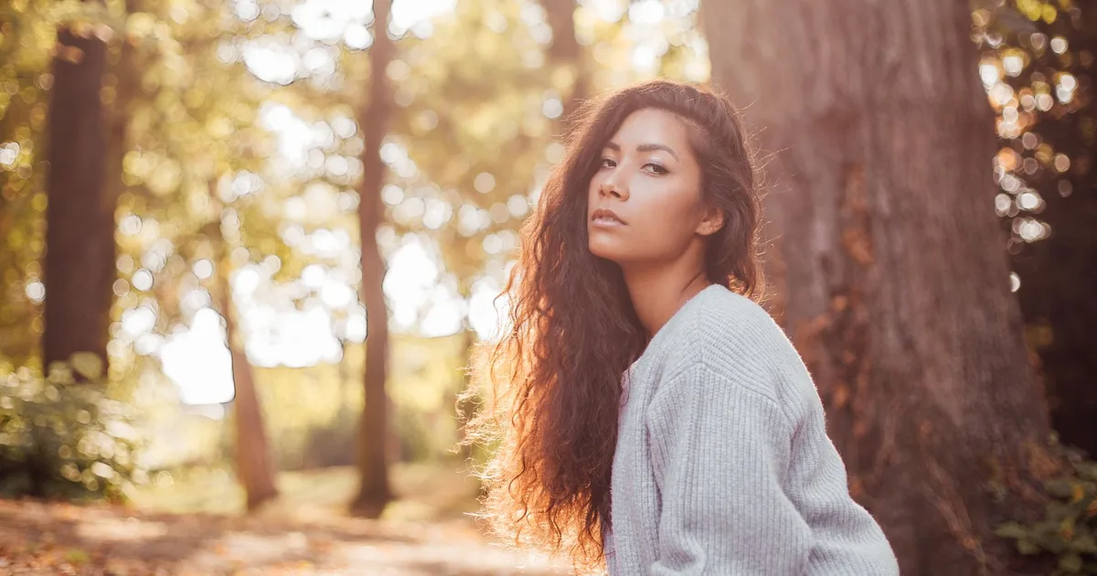 A serene portrait of a woman in a sunlit autumn forest, showcasing natural beauty.