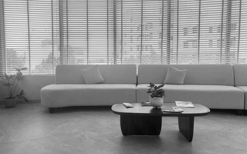A stylish, minimalist living room featuring a large sofa, coffee table, and wide windows with blinds.