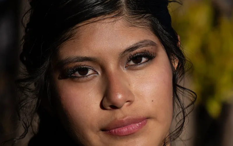A close-up portrait of a young woman with natural beauty in soft lighting outdoors.