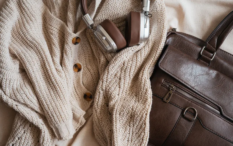 Warm fashion flat lay with knit cardigan, headphones, and leather bag.