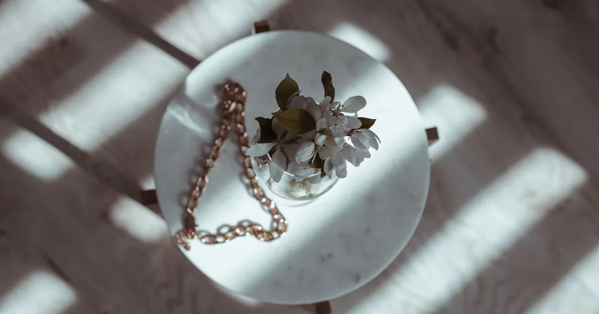 Stylish flat lay featuring a white floral bouquet and a chain on a round table with dramatic shadows.