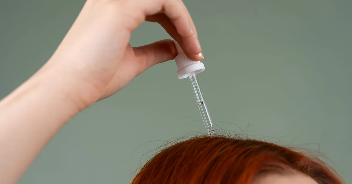 Close-up of hand applying hair serum on red hair with a dropper.