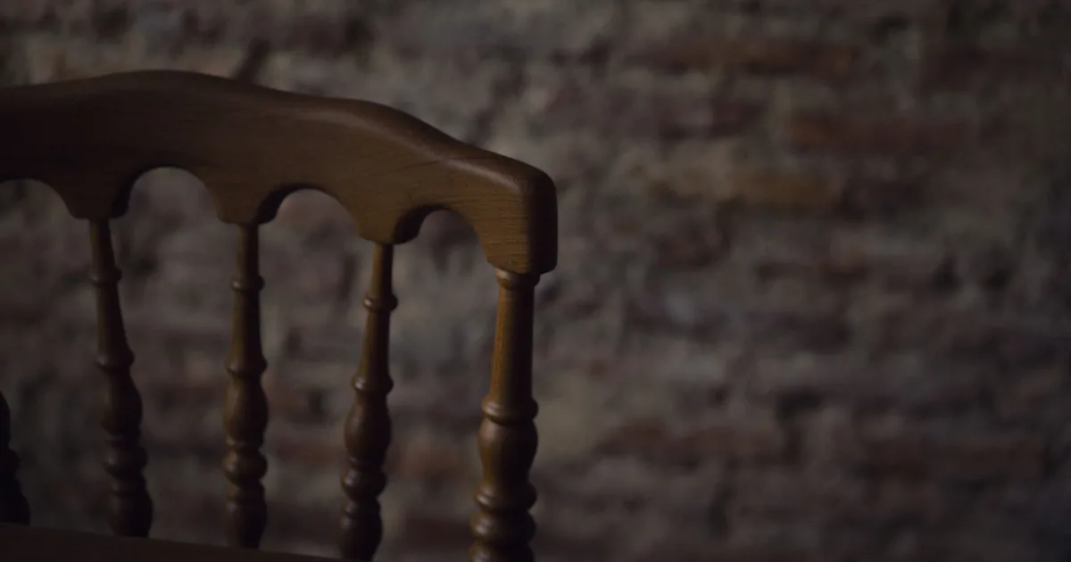 Close-up of an antique wooden chair with a textured, rustic brick wall background.