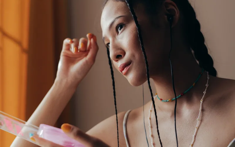 Portrait of a woman with braided hair and colorful necklace, captured indoors with natural lighting.