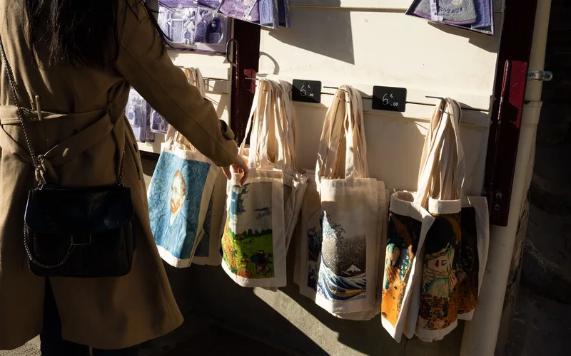 A woman shopping for artistic tote bags at a street market in Arles, France.