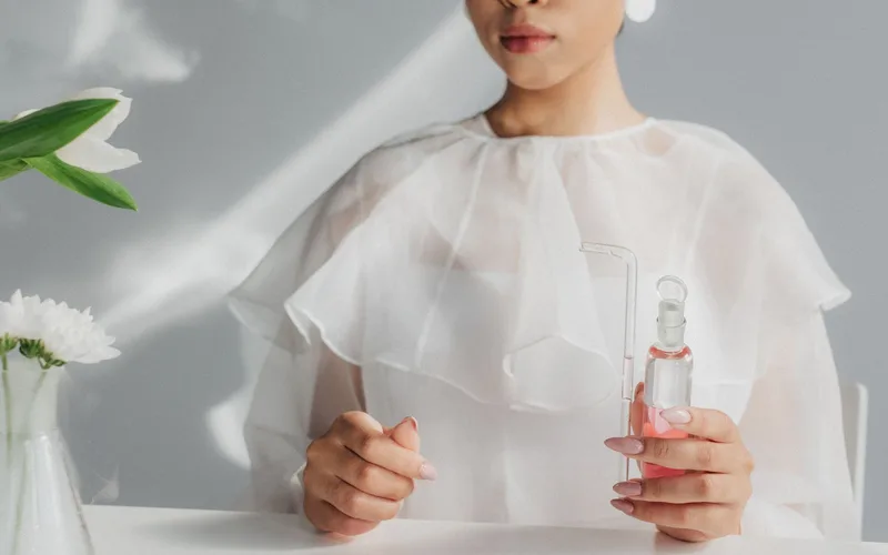 Woman in white blouse holding a glass flask in a minimalist laboratory environment.