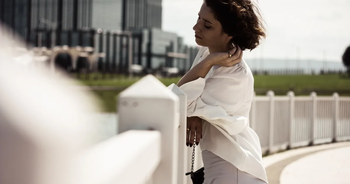Elegant woman poses by a railing with modern architecture in the background, embodying contemporary style and grace.