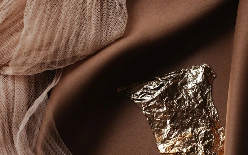 Artistic composition featuring draped fabrics and a piece of gold foil on a dark backdrop.