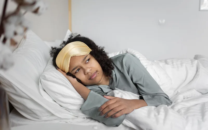 Cozy scene of a woman lying in bed with an eye mask, contemplating and relaxing.