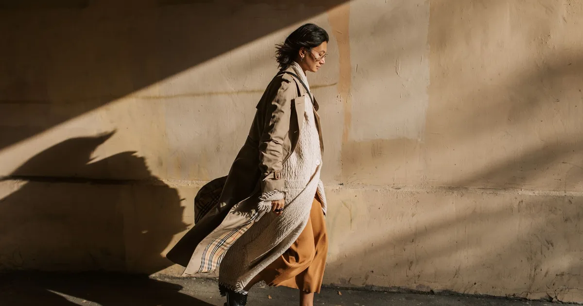 Side view of a stylish woman in a trench coat walking in sunny autumn weather.
