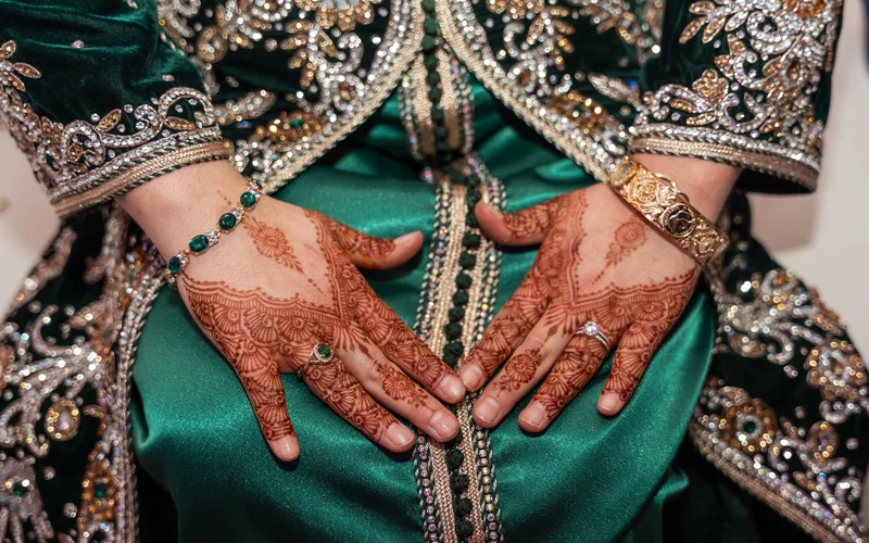 Close-up of hands with henna, adorned in elaborate green traditional attire with jewelry.