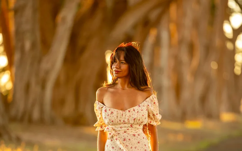 A woman in a floral dress stands on a sunlit forest path, embracing nature's tranquility.
