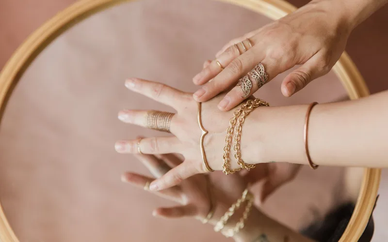 Close-up of elegant hands with jewelry, reflecting on a mirror surface.