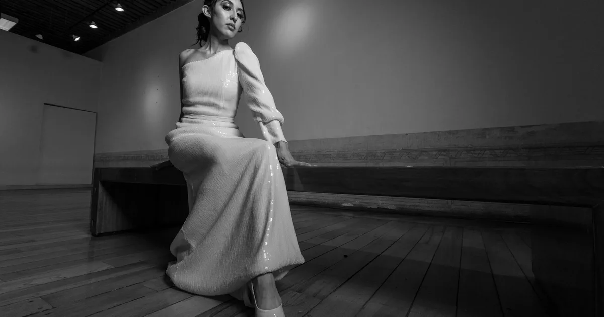A striking black and white portrait of an elegant woman in a long white dress sitting indoors.
