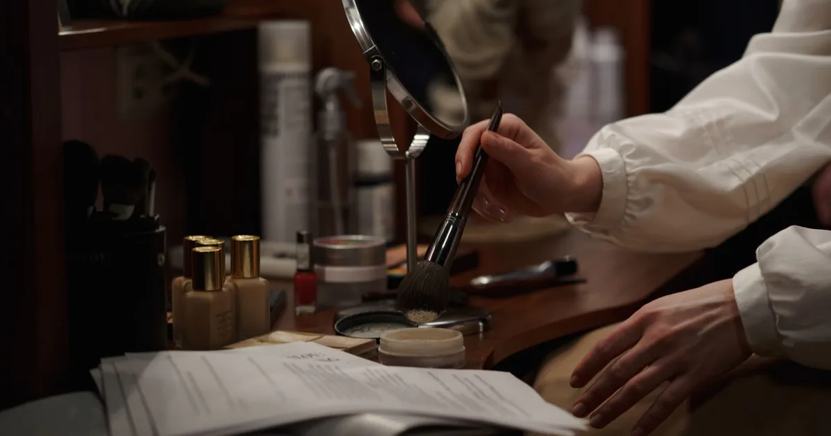 A woman applies makeup in a dressing room, focusing on artistry and glamour backstage.