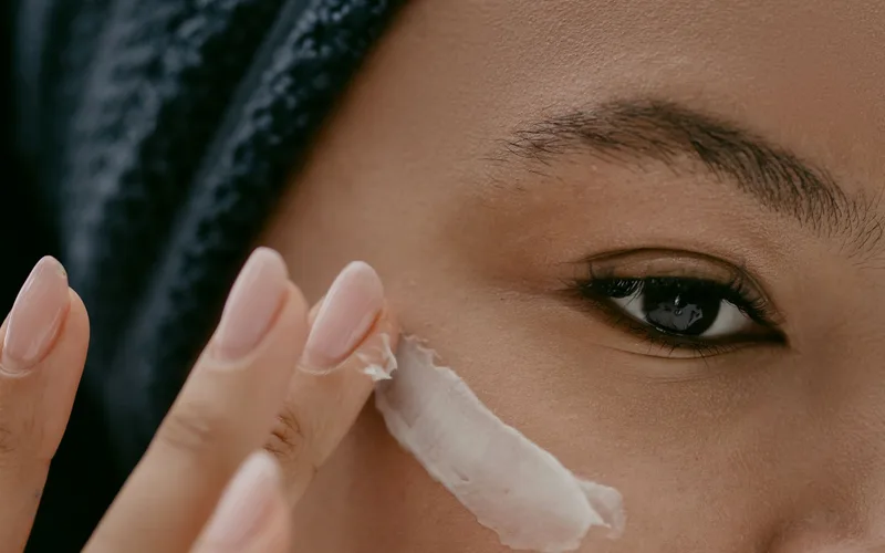 Extreme close-up of a woman applying cream to her cheek for healthy skin care.