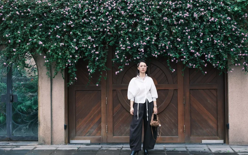 Stylish woman in elegant attire standing before a wooden door adorned with floral vines.
